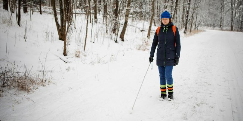 Valkoisen kepin käyttäjä lumisella kävelytiellä.